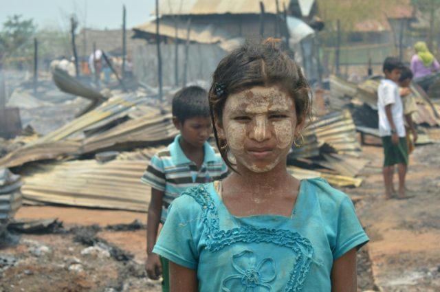 Rohingya children look on past charred shelters following a fire that gutted the Bawdupa c