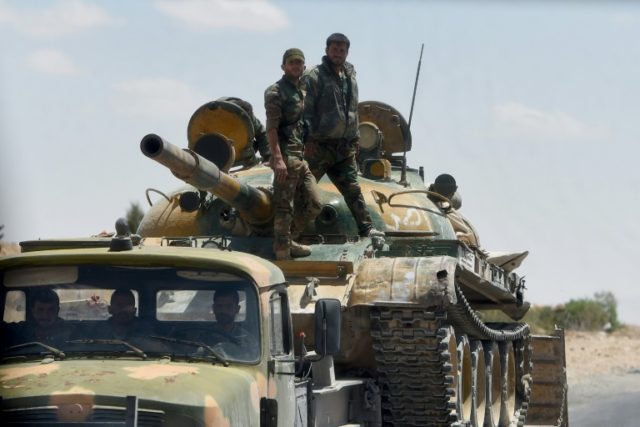 Syrian soldiers stand on a tank loaded on a lorry as they patrol near the ancient city of