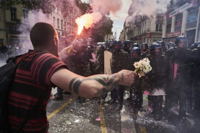 A man holds flowers and a torch as he faces riot police during a demonstration against the