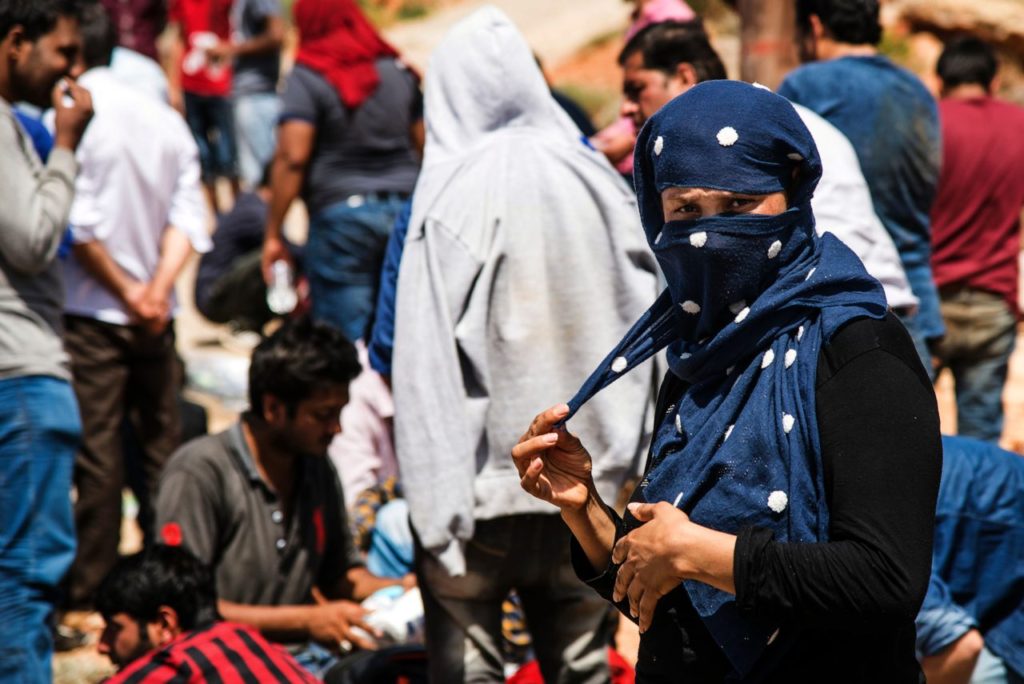A woman pulls a corner of her headscarf as she stands with refugees and migrants upon their arrival with a boat near the village of Finokalia in the southern Greek island of Crete on May 31, 2016. More than 2,500 people have died trying to make the perilous journey across the Mediterranean sea to Europe so far in 2016, the UN said on May 31, a sharp jump from the same period last year. At the same time some 204,000 migrants and refugees have crossed the Mediterranean to the continent since January, a figure that has also climbed acutely.   / AFP / STR        (Photo credit should read STR/AFP/Getty Images)