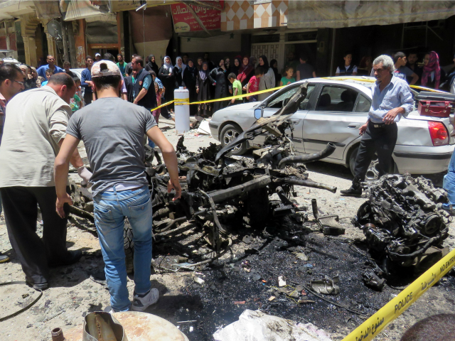 Syrians look at a burnt out vehicle used in a double bombing attack on June 11, 2016 outsi
