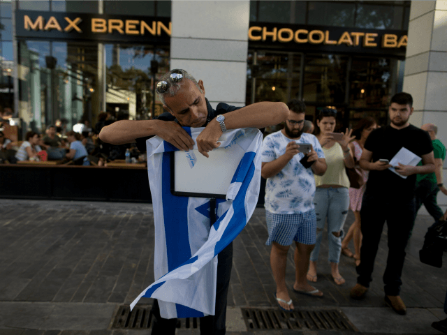An Israeli man hungs an Israeli flag outside Max Brenner restaurant in Sarona Market on Ju