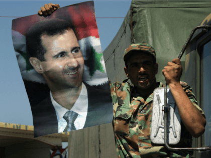 A Syrian soldier waves a picture of the Syrian president, Bashar Assad, as he crosses the