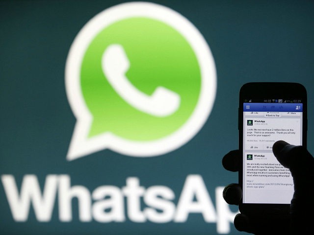 A Whatsapp App logo is seen behind a Samsung Galaxy S4 phone that is logged on to Facebook