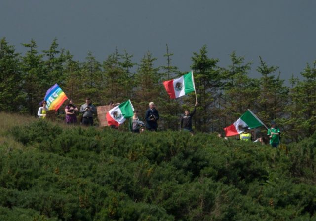 A group of protesters wave Mexican flags on the hillside above the Trump International Gol