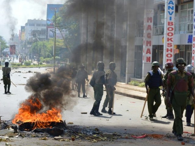Police officers walk past burning tyres in Kisumu, Kenya, on June 6, 2016