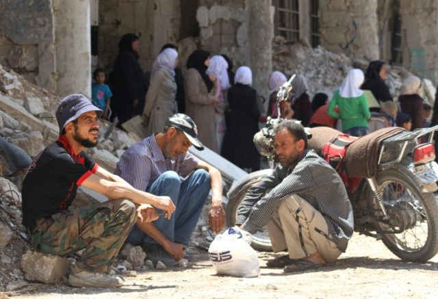 Syrian men sit next to a damaged building in the town of Daraya, southwest of Damascus, on