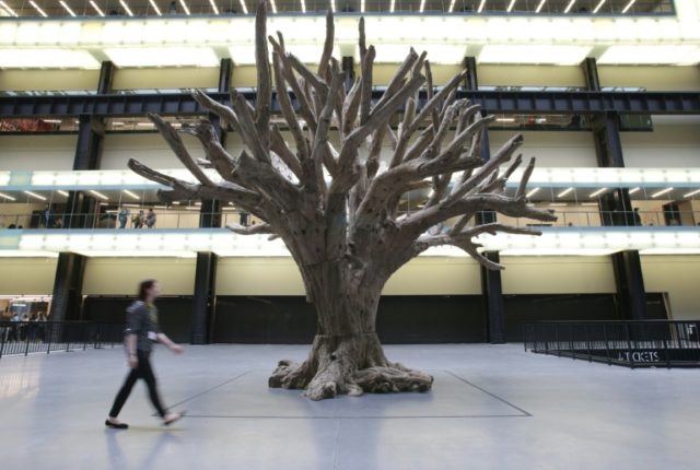 A visitor poses for a picture next to the 'Tree, 2015' by Chinese artist Ai Weiwei in the