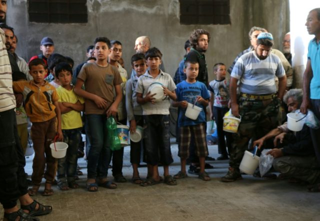 Syrians wait to receive meals distributed by the "Syria charity" NGO to impoverished famil