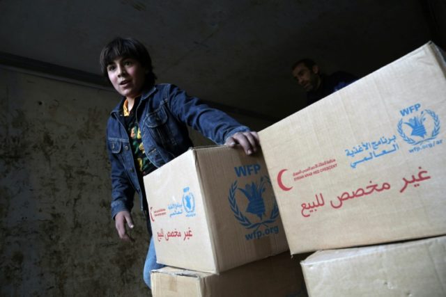 A child walks past boxes of aid provided by the World Food Programme (WFP) in Kafr Batna,