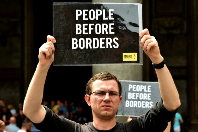 A man holds a placard reading "People Before Borders" in front of the Pantheon in central