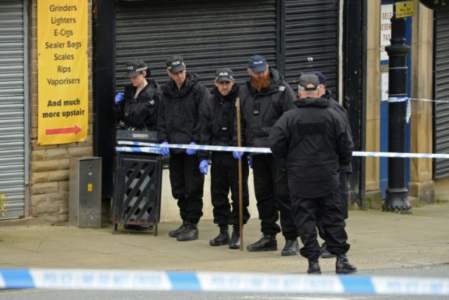 Police officers search the area near the crime scene outside the library in Birstall, nort
