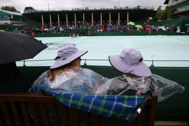 Spectators with umbrellas and rain gear sit alongside outer courts with the rain covers on