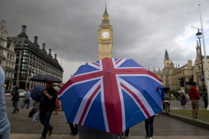 A pedestrian shelters from the rain beneath a Union Jack-themed umbrella near the Houses of Parliament in central London