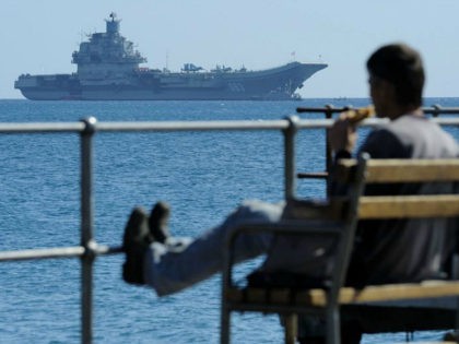 A man enjoy the sea and the sun as in the background the Russian aircraft carrier Admiral Kuznetsov lies at anchor off Cyprus’ largest port of Limassol on Thursday, Feb. 27, 2014. The aircraft carrier arrived in Cyprus for a three-day rest and resupply stay. (AP Photo/Pavlos Vrionides)