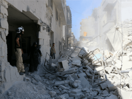 Syrians look at civil defence workers using a digger to look for survivors in the rubble o