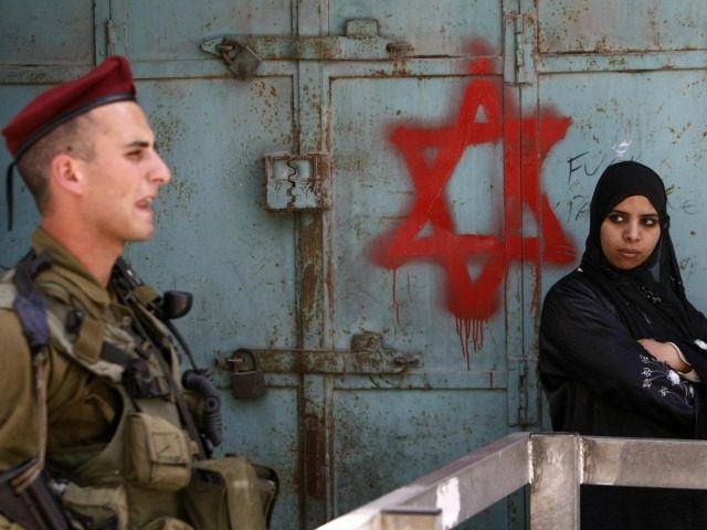 An Israeli soldier keeps guard near a Palestinian woman standing by a Star of David graffi