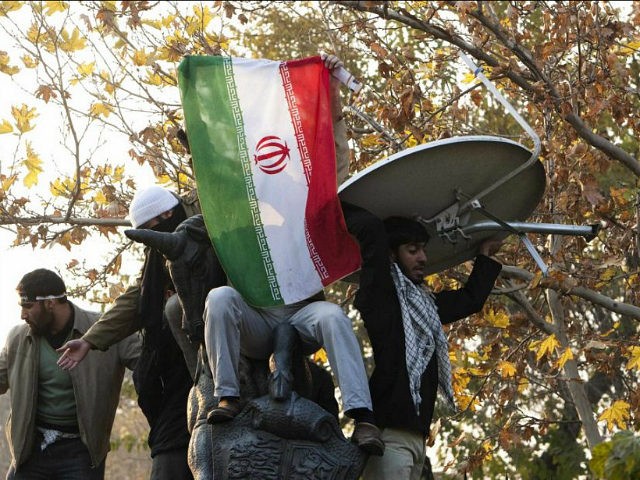 Iranian protesters remove a satellite dish from a building near the gate of the British Em