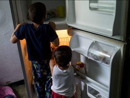 Young childern look in an empty refrigerator at a home in the Catia neighborhood on the ou