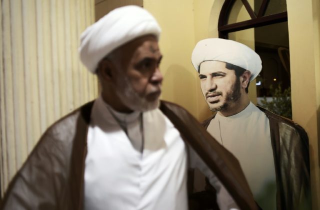 A Bahraini cleric walks past a cardboard cutout bearing the portrait of Sheikh Ali Salman,