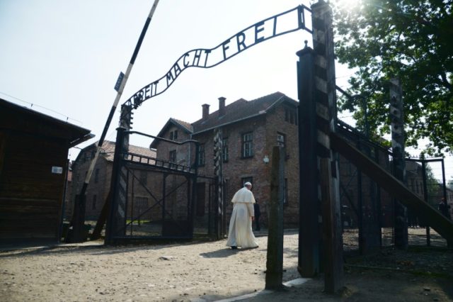 Pope Francis walks alone through the main gate at Auschwitz with its lettering "Arbeit Mac