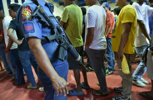 A Philippine policeman (L) stands guard as people queue to register with the police during