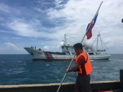 A Filipino activist holds a Philippine flag on a ship while a Chinese coast guard ship sai