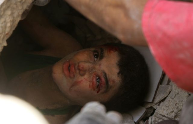 A Syrian boy trapped under the rubble of buildings looks up as civil defence volunteers tr