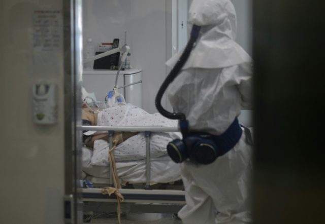A medical staff member wearing a protective suit enters the room of a patient suffering fr