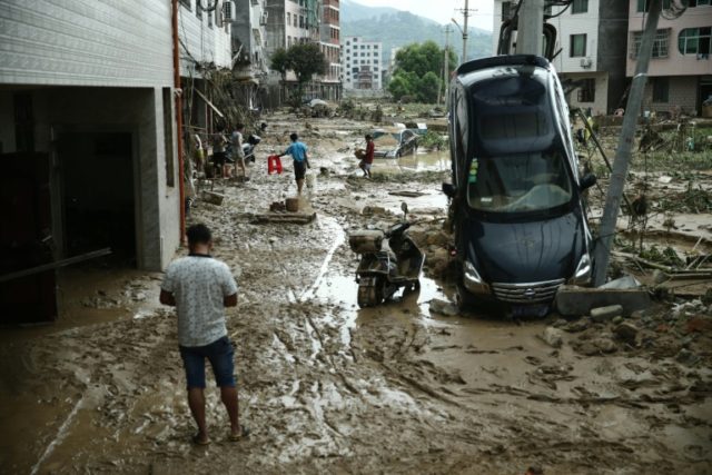 Residents walk past a damaged car in the aftermath of a tropical storm in Bandong town, in