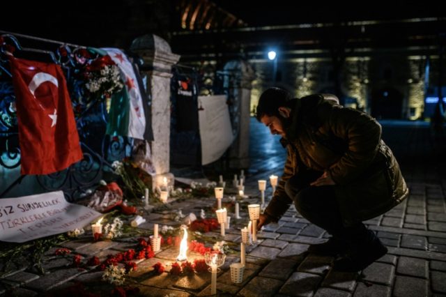 A man lights a candle at a makeshift memorial with flowers and a Turkish and a Syrian flag