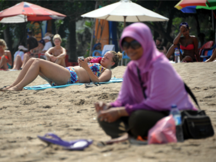 A Muslim woman wearing a veil sits in front of foreign tourists wearing bikinis on Kuta be