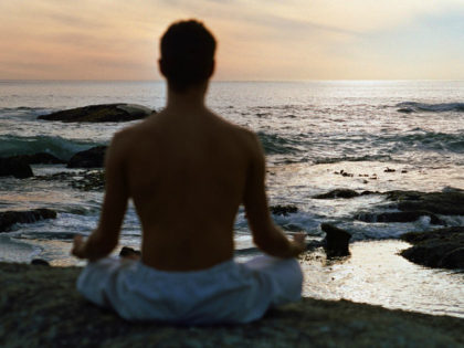 Man sitting in lotus position in front of sea, rear view, silhouette.