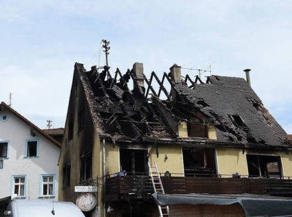 Two men stand on a lifting platform next to a burnt out shelter for asylum seekers in Goes