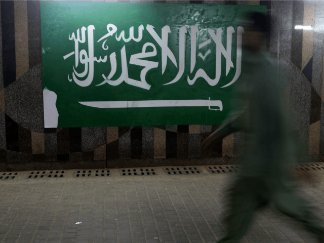 A man walks beside the Saudi flag at the popular market of Qabil street in the heart of Je