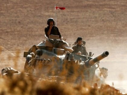 Turkish soldiers hold their position on a tank as they watch the town of Kobani from near