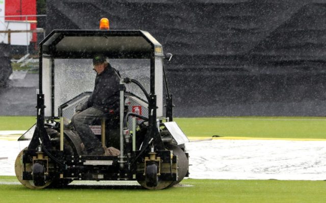 Ground staff work to clear water as wind and rain hold up play before the second one-day i
