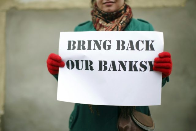 A woman holds a placard that reads "Bring Back Our Banksy" during a protest next to a sect