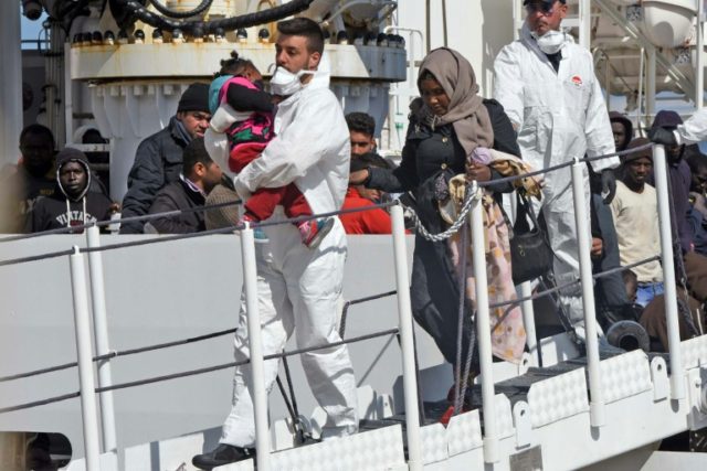 A rescuer carries a baby as migrants and refugees arrive in the port of Messina following