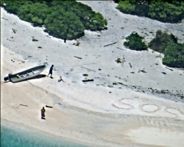A US Navy photo shows two people signalling for help by writing "SOS" in the sand on Augus