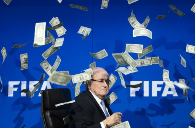 Former FIFA president Sepp Blatter looks on as fake dollar notes fly around him, thrown by