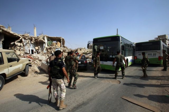 Syrian troops stand guard as a bus carrying people drives by, as part of an evacuation fro