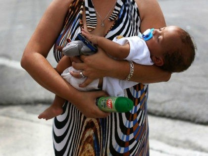 MIAMI, FL - AUGUST 02: Barbara Betancourt holds her baby Daniel Valdes after being given a can of insect repellent by James Bernat, a City of Miami police officer, as he helps people living around the Miami Rescue Mission prevent mosquito bites that may infect them with the Zika virus …