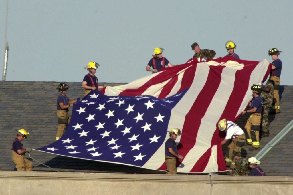 Military and fire personnel get set to unfurl a large American flag on the roof of the Pentagon, Wednesday, Sept. 12, 2001. A hijacked airliner crashed into the structure on Tuesday. (AP Photo/Steve Helber)