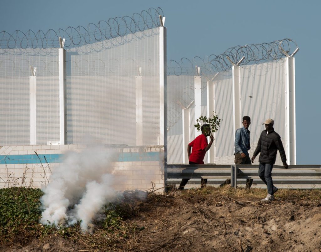 Migrants run away from tear gas during clashes with riot police trying to prevent them from getting into trucks heading to Great Britain, on September 21, 2016 in Calais. / AFP / PHILIPPE HUGUEN (Photo credit should read PHILIPPE HUGUEN/AFP/Getty Images)
