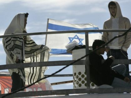 The Israeli flag flutters as settlers one in a prayer shawls or Talit bunker down on the roof of one of the nine houses marked for destruction in the Amona settlement in the West Bank, northeast of the town of Ramallah, 31 January 2006.