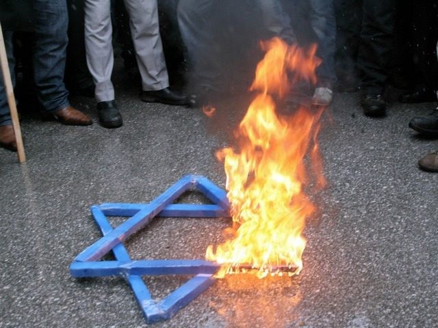 Protesters shout slogans as a Star of David burns at a protest against Israeli attacks on