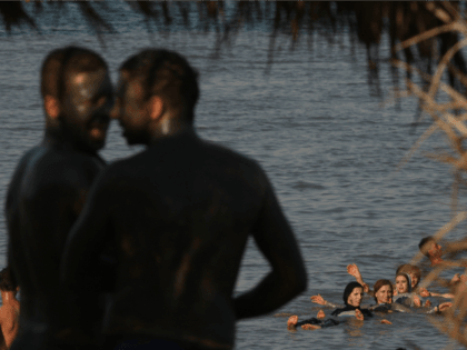 Two Palestinian youths cover their bodies with mineral-rich mud as a group of women swim i