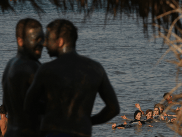 Two Palestinian youths cover their bodies with mineral-rich mud as a group of women swim i