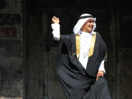 An elderly Palestinian man wearing traditional clothes throws a stone towards Israeli secu